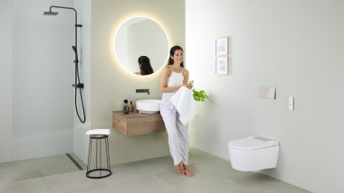 Femme appuyée sur un lavabo dans une salle de bains avec douche Geberit AquaClean Sela, lavabo Geberit VariForm et meubles.