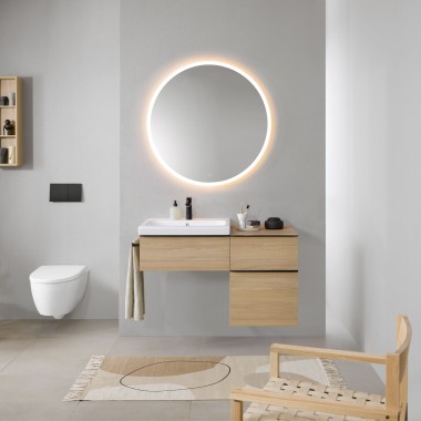 Salle de bains avec murs gris, meubles de salle de bains Geberit en bois et miroir rond Geberit Option éclairé