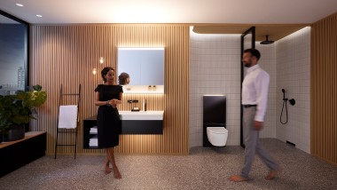 Homme et femme dans une salle de bains parfaitement éclairée avec les meubles de salle de bains et les céramiques sanitaires Geberit ONE (© Geberit)