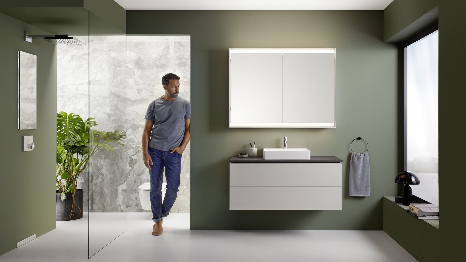 Homme debout dans une salle de bains présentant la ligne de salles de bains Geberit ONE Homme debout dans une salle de bains présentant la ligne de salles de bains Geberit ONE