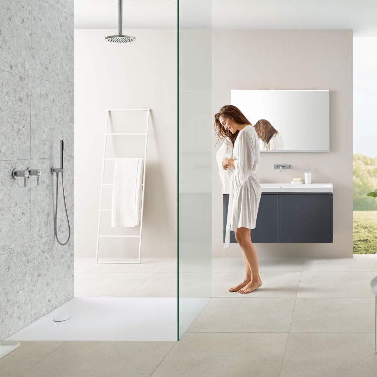 Femme dans une salle de bains avec douche à l’italienne et receveur de douche Geberit Olona Femme dans une salle de bains avec douche à l’italienne et receveur de douche Geberit Olona