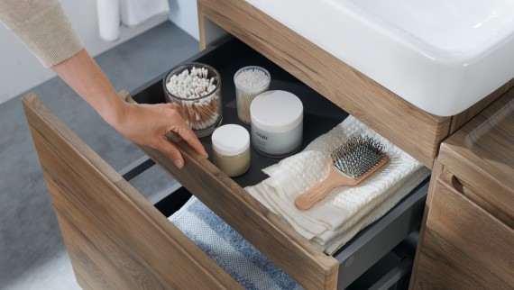 Une main ouvre l'un des tiroirs du meuble lavabo Geberit Renova Plan en bois naturel.