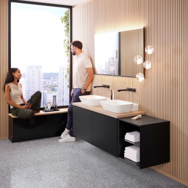 Femme assise sur le rebord d’une fenêtre parlant à un homme dans une salle de bains design, Geberit ONE Femme assise sur le rebord d’une fenêtre parlant à un homme dans une salle de bains design, Geberit ONE