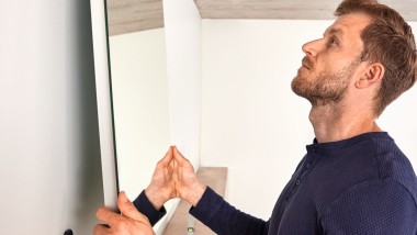 Un homme accroche un miroir Geberit Option pendant la rénovation de la salle de bains