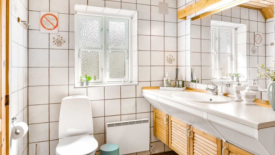 La salle de bains dʼorigine avec WC au sol, carrelage blanc et meubles de salle de bains en bois (© @triner2 et @strandparken3)