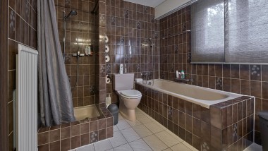 La salle de bains avec coin douche étroit, baignoire et WC au sol