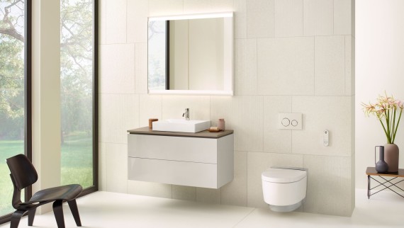 Salle de bains beige avec armoire de toilette, meuble sous lavabo, plaque de déclenchement et céramiques sanitaires de Geberit