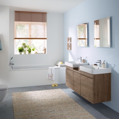 Salle de bains familiale avec mur bleu clair et meubles de salle de bains, miroir, plaque de déclenchement et appareil en céramique Geberit