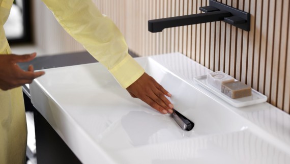 Une femme retire le filtre à cheveux sur un lavabo Geberit ONE avec robinet en noir mat. (© Geberit) Une femme retire le filtre à cheveux sur un lavabo Geberit ONE avec robinet en noir mat. (© Geberit)