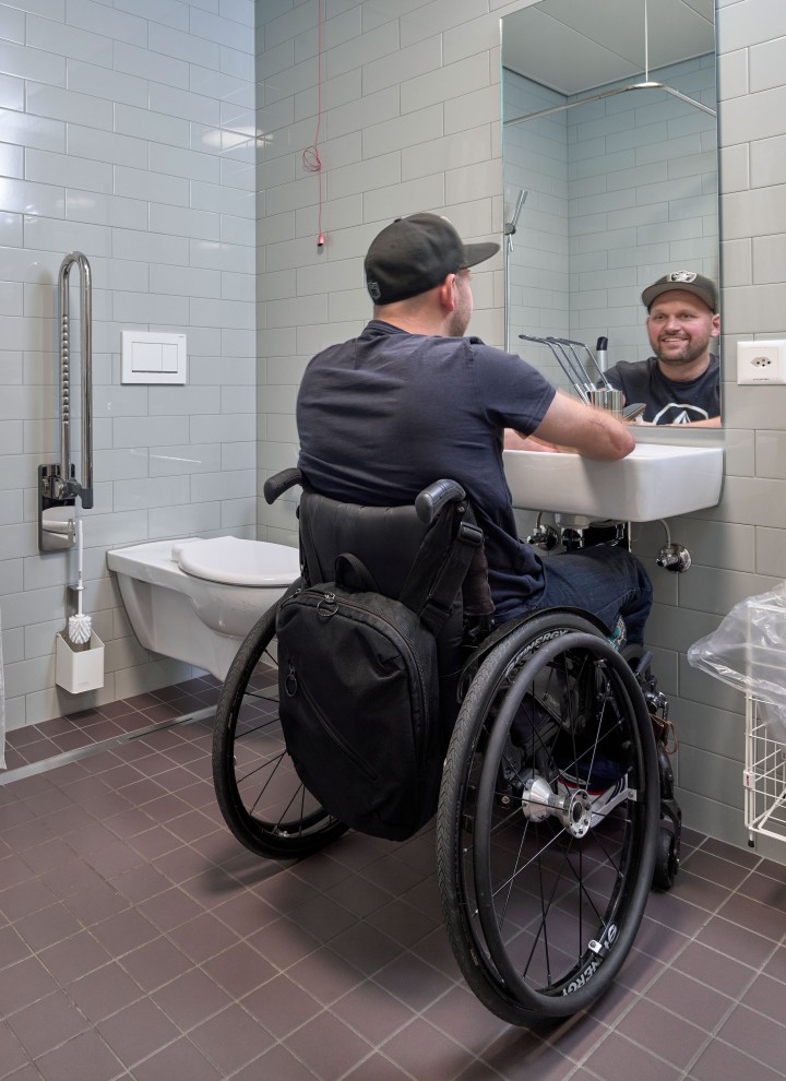 Peter Roos en fauteuil roulant au niveau de la zone de lavage dans une salle de bains adaptée PMR (© Ben Huggler) Peter Roos en fauteuil roulant au niveau de la zone de lavage dans une salle de bains adaptée PMR (© Ben Huggler)
