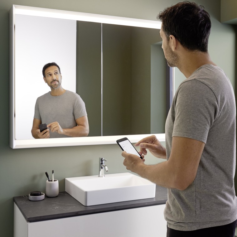 Un homme commande lʼéclairage de lʼarmoire de toilette Geberit ONE avec son smartphone (© Geberit) Un homme commande lʼéclairage de lʼarmoire de toilette Geberit ONE avec son smartphone (© Geberit)