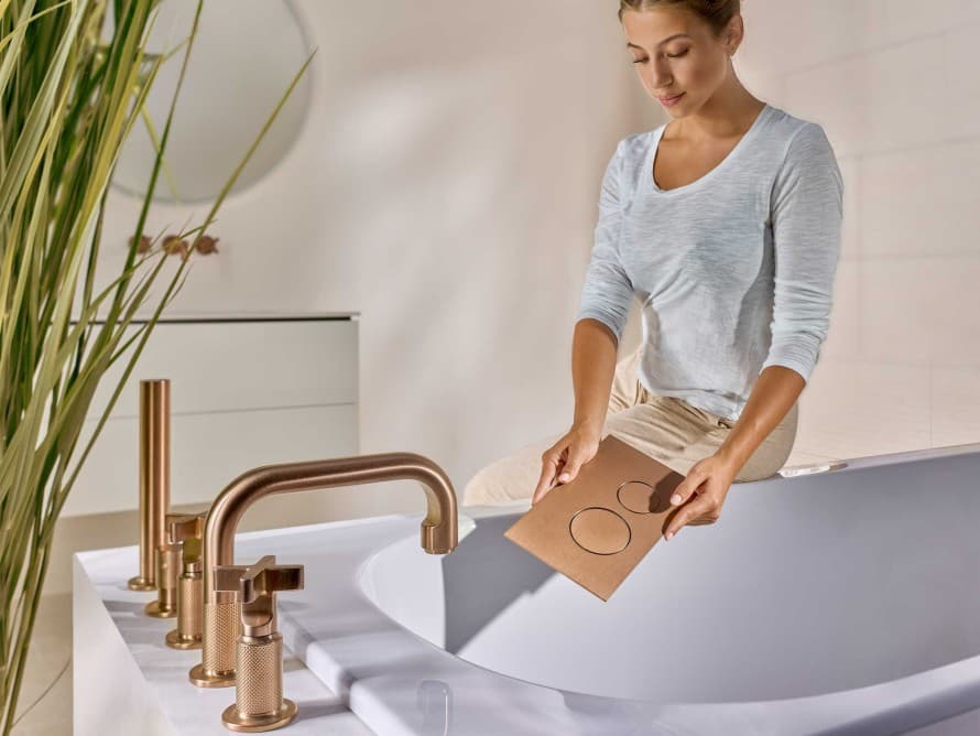 Femme dans la salle de bains avec une plaque de déclenchement Sigma40 en cuivre brossé, assortie à la robinetterie