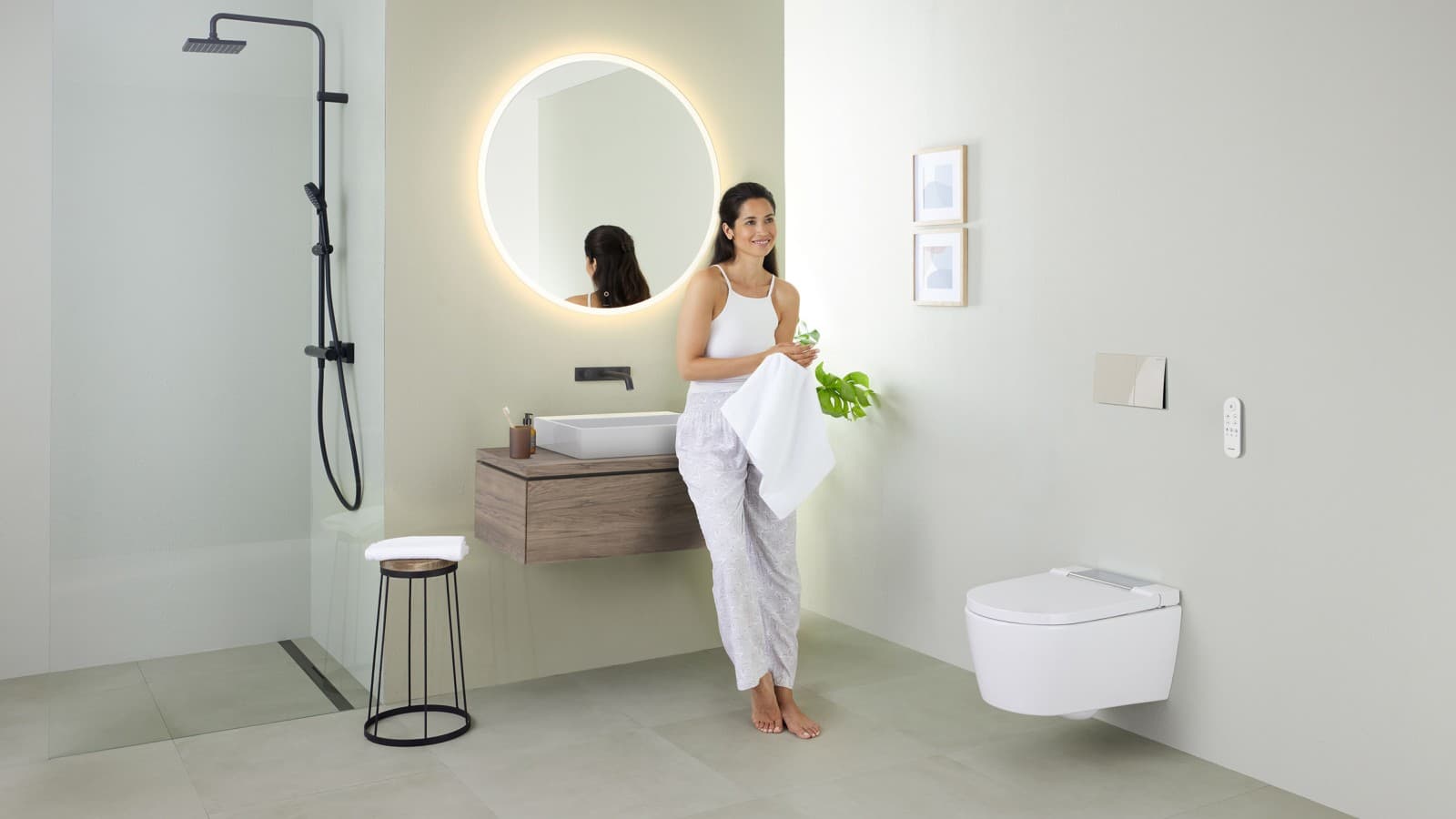 Femme appuyée sur un lavabo dans une salle de bains avec WC lavant Geberit AquaClean Sela Femme appuyée sur un lavabo dans une salle de bains avec WC lavant Geberit AquaClean Sela