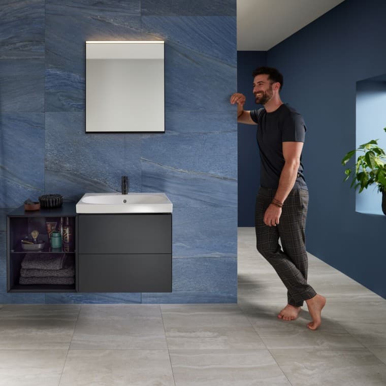 Homme adossé au mur dans une salle de bains bleue avec un lavabo Geberit Mix & Match Homme adossé au mur dans une salle de bains bleue avec un lavabo Geberit Mix & Match